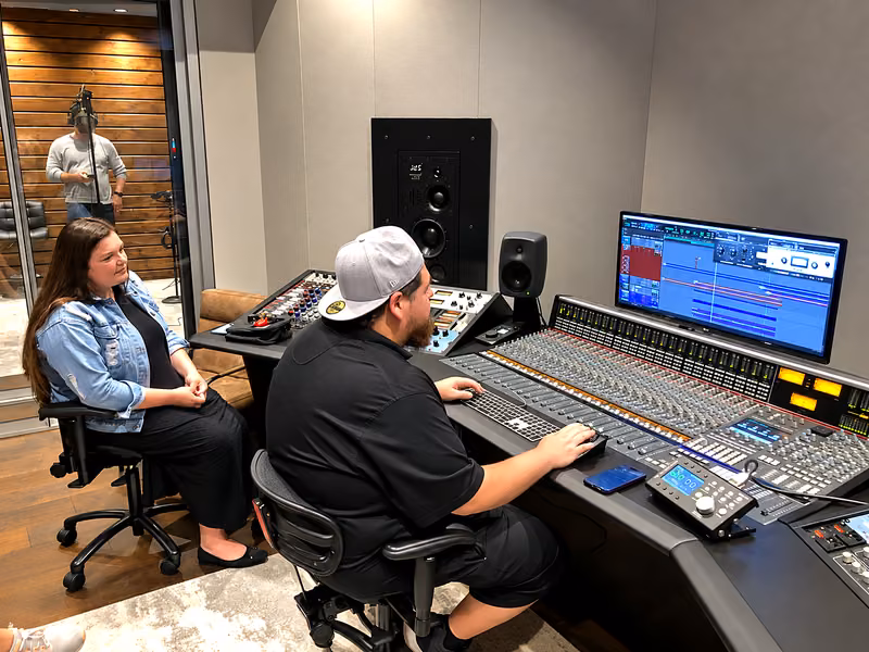 Ro running a recording session at the console while an artist sings in the booth