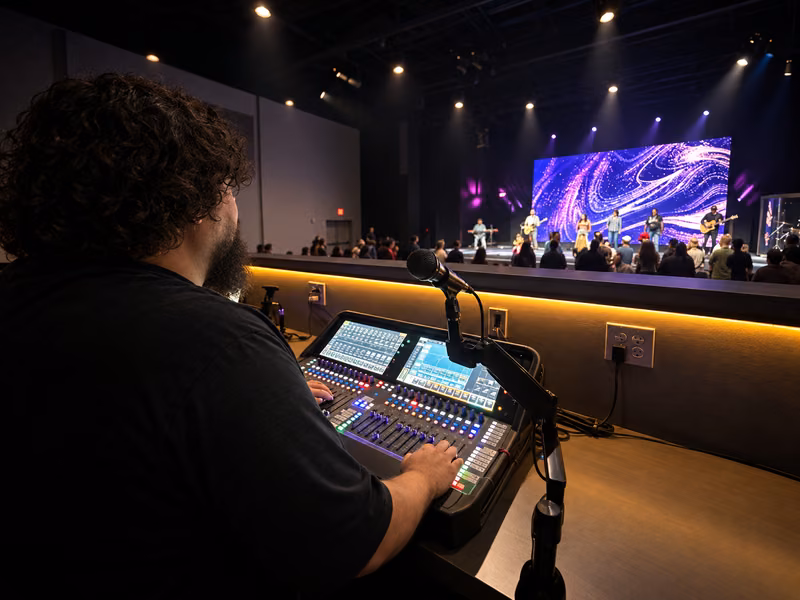 Ro mixing at a church sound console while the worship team plays on a lit stage